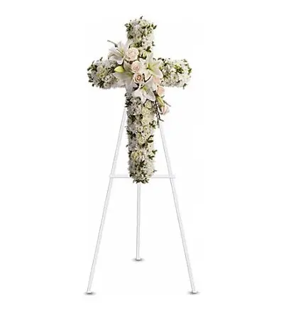 White floral cross of lilies and cream roses on a white easel