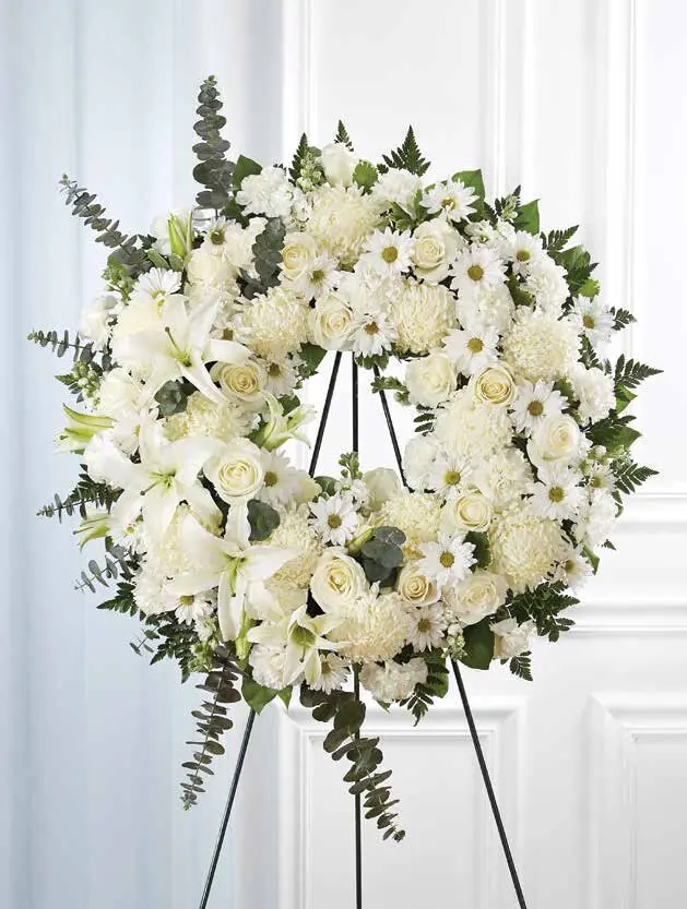 White standing wreath of lilies, roses, mums and daisies on an easel