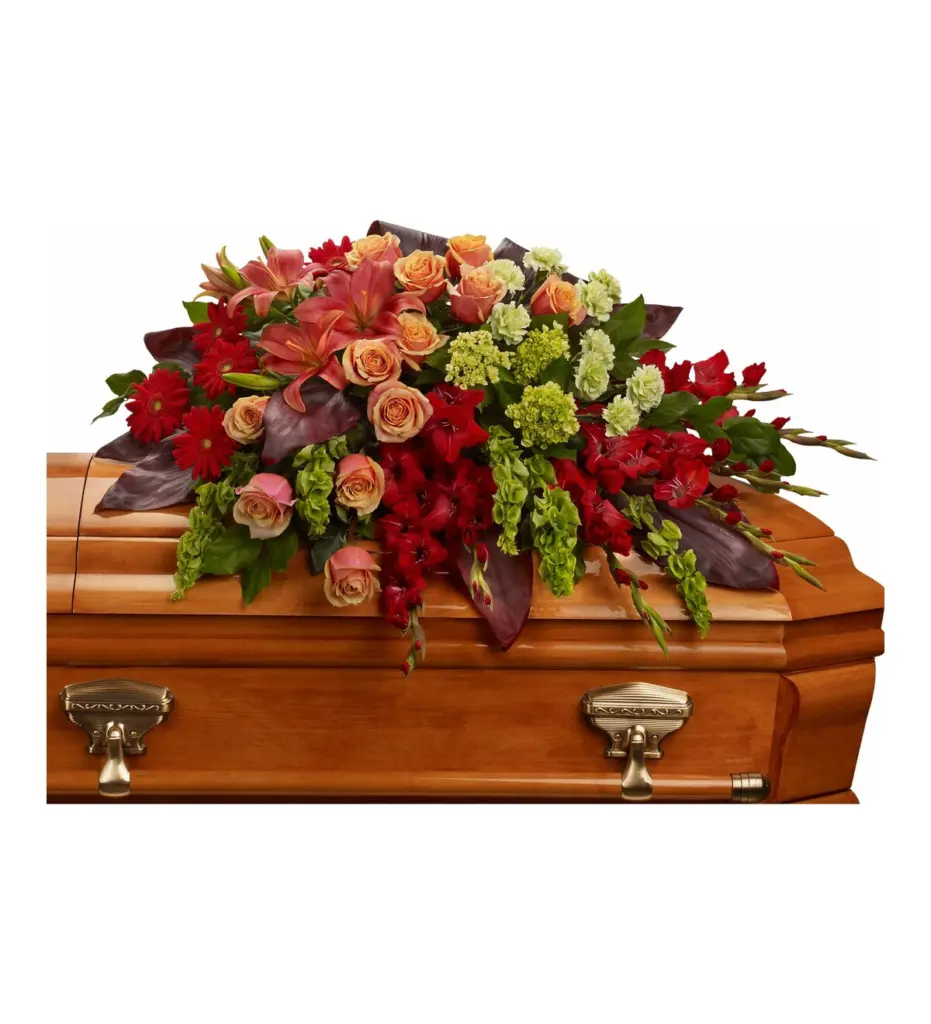 Peach, coral and red casket spray with roses, lilies and gladiolus on a wooden casket