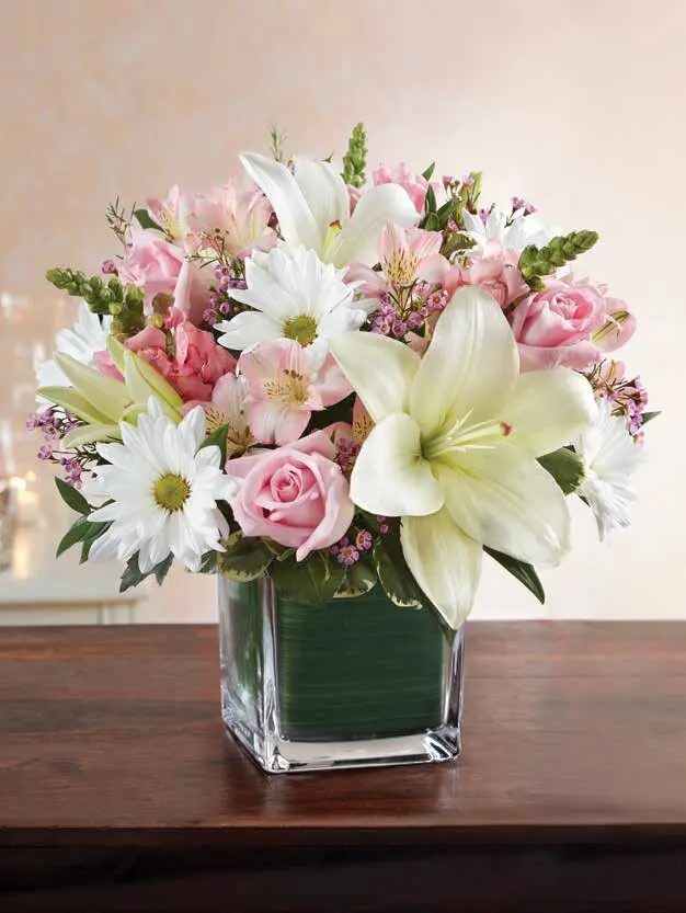 Pink roses, white lily and daisies in a leaf-lined glass cube vase