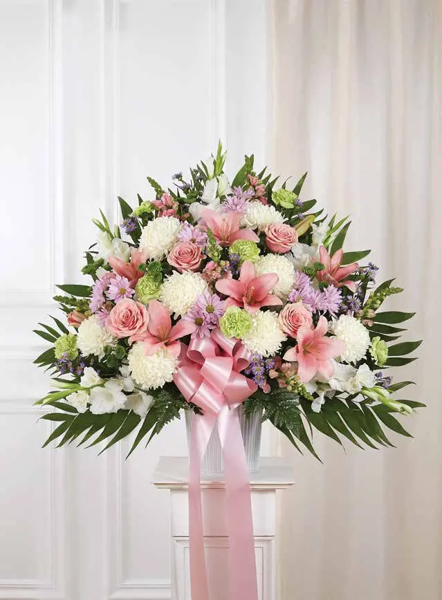Pink and white basket of lilies, roses and mums on a white pedestal