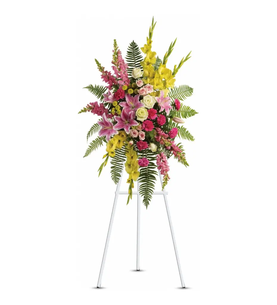 Pink and yellow standing spray of lilies, gladiolus, snapdragons and roses on white easel