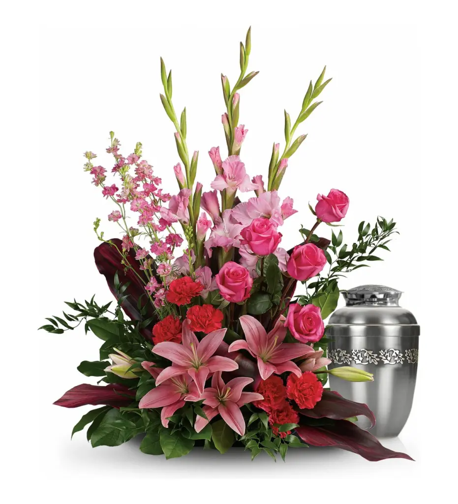Pink roses, lilies and gladiolus arranged beside a silver urn with a leaf band