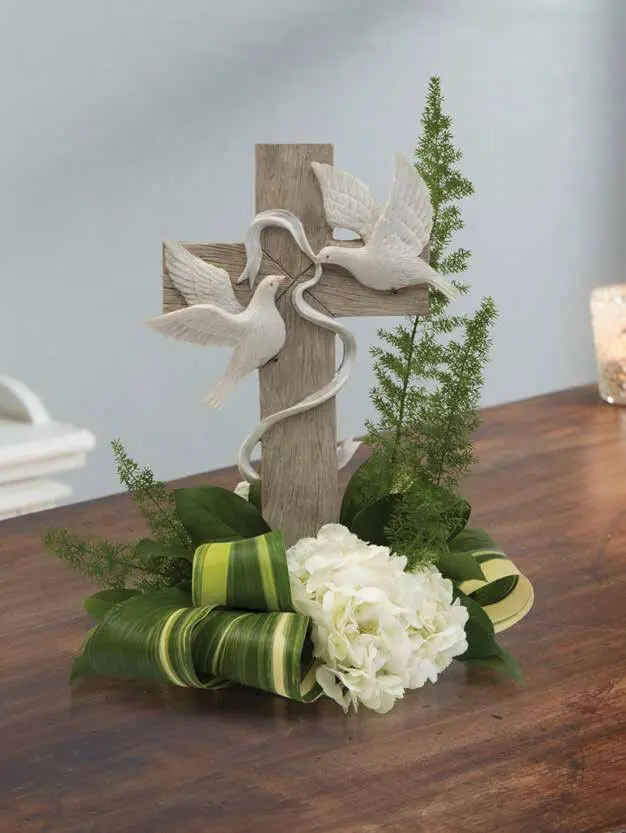 White hydrangea and fern at the base of a wooden cross with two doves