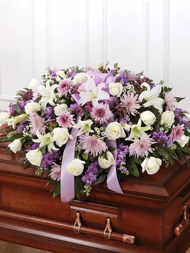 Lavender and white half casket spray of roses and lilies on a wooden casket