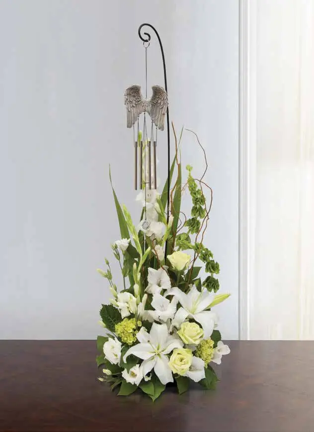 White lilies and green roses beneath an angel-wing wind chime on a shepherd's hook